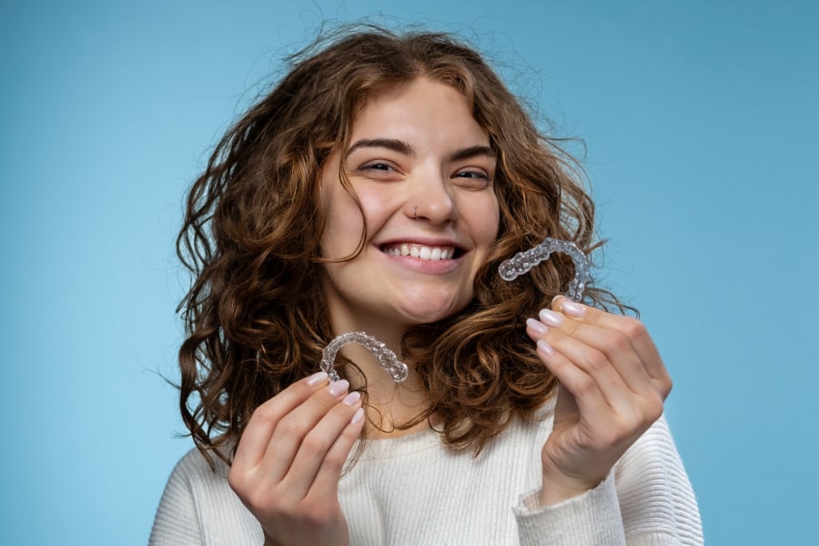 A girl is holding Invisalign aligners and smiling