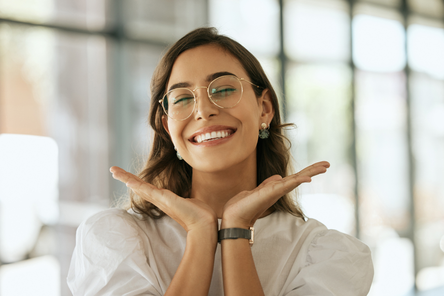A woman is joyfully smiling with two hands near her face