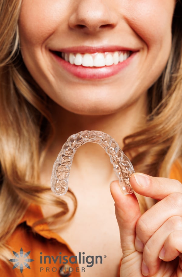 A woman is smiling and holding Invisalign aligners in her hands